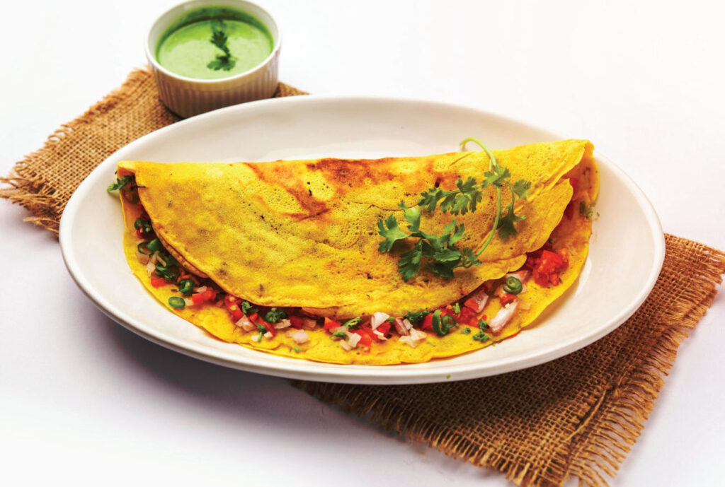 Vegetable stuffed omelette placed in a white plate with chutney.