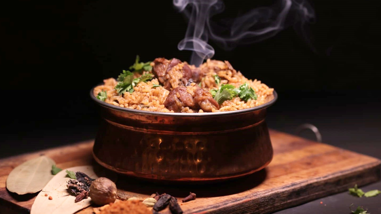 A bowl of Kongu Mutton Biryani placed on a wooden board with a few spices