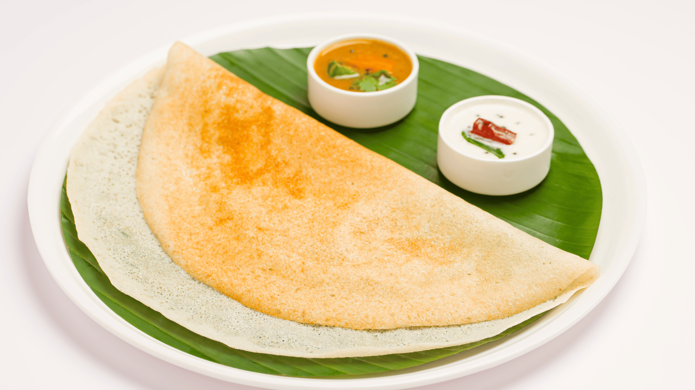 Dosa served in plate covered by banana leaf with sambhar and chutney