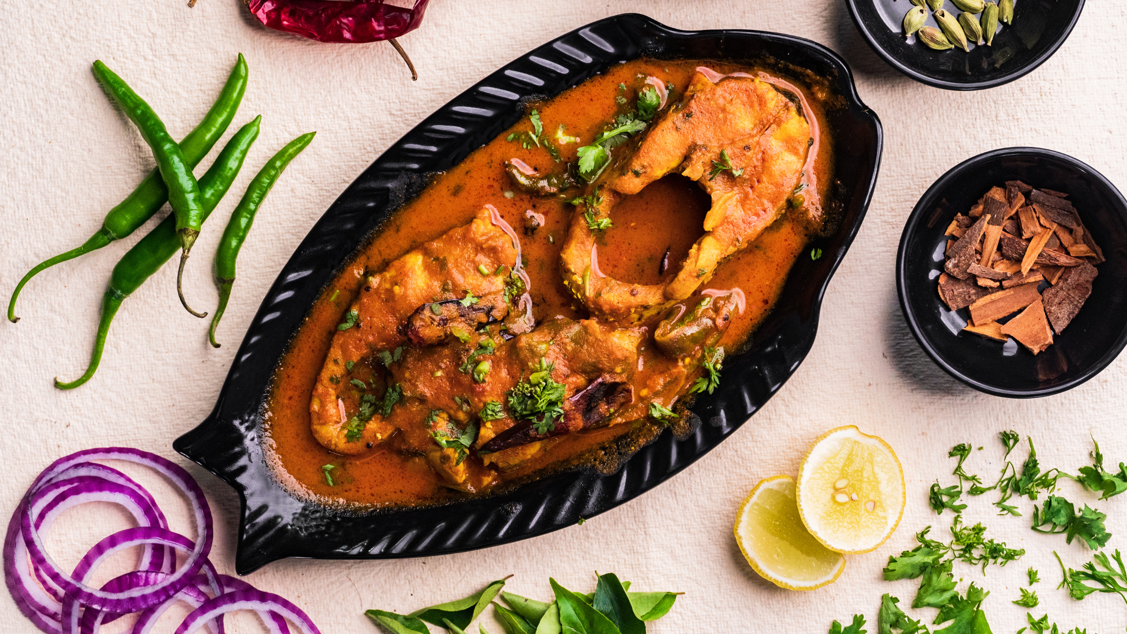 Fish curry served in fish shaped bowl with Indian spices around