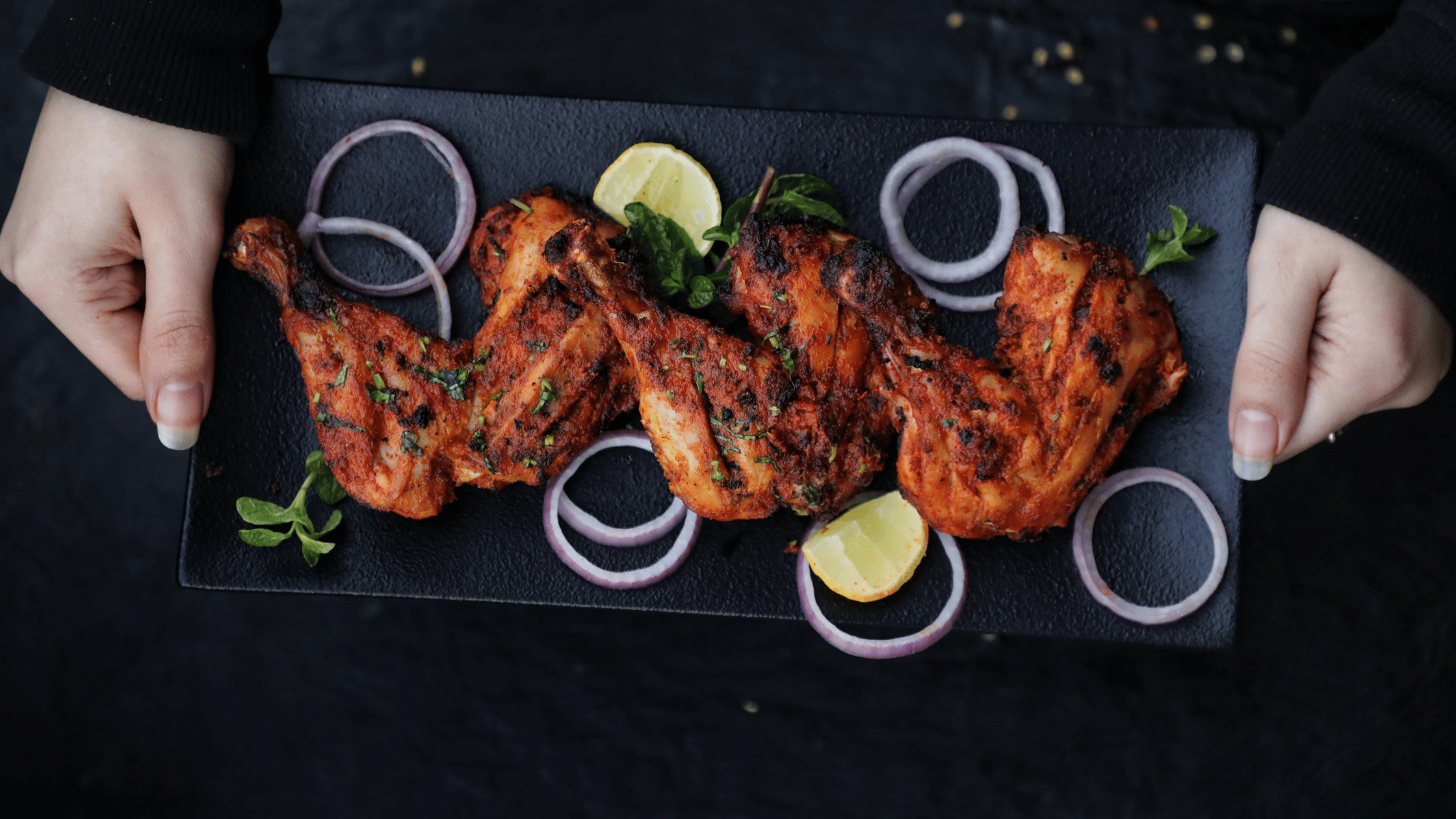 Man holding a plate of chicken tandoori with sliced onion and lemon.