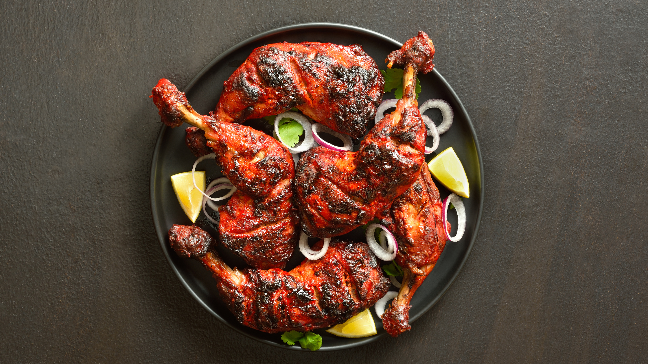 Chicken Tandoori served in a Black plate with slices of lemon and onion