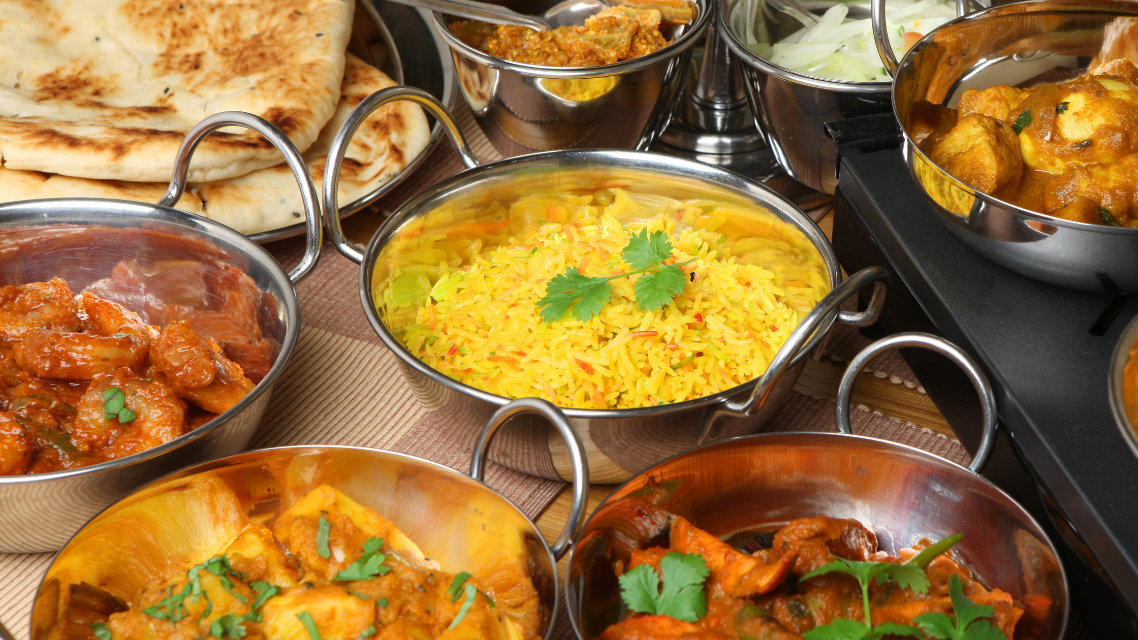 Group of indian food served in the stainless steel tawa. The foods are Nan, Ghee Rice, and Paneer Masala