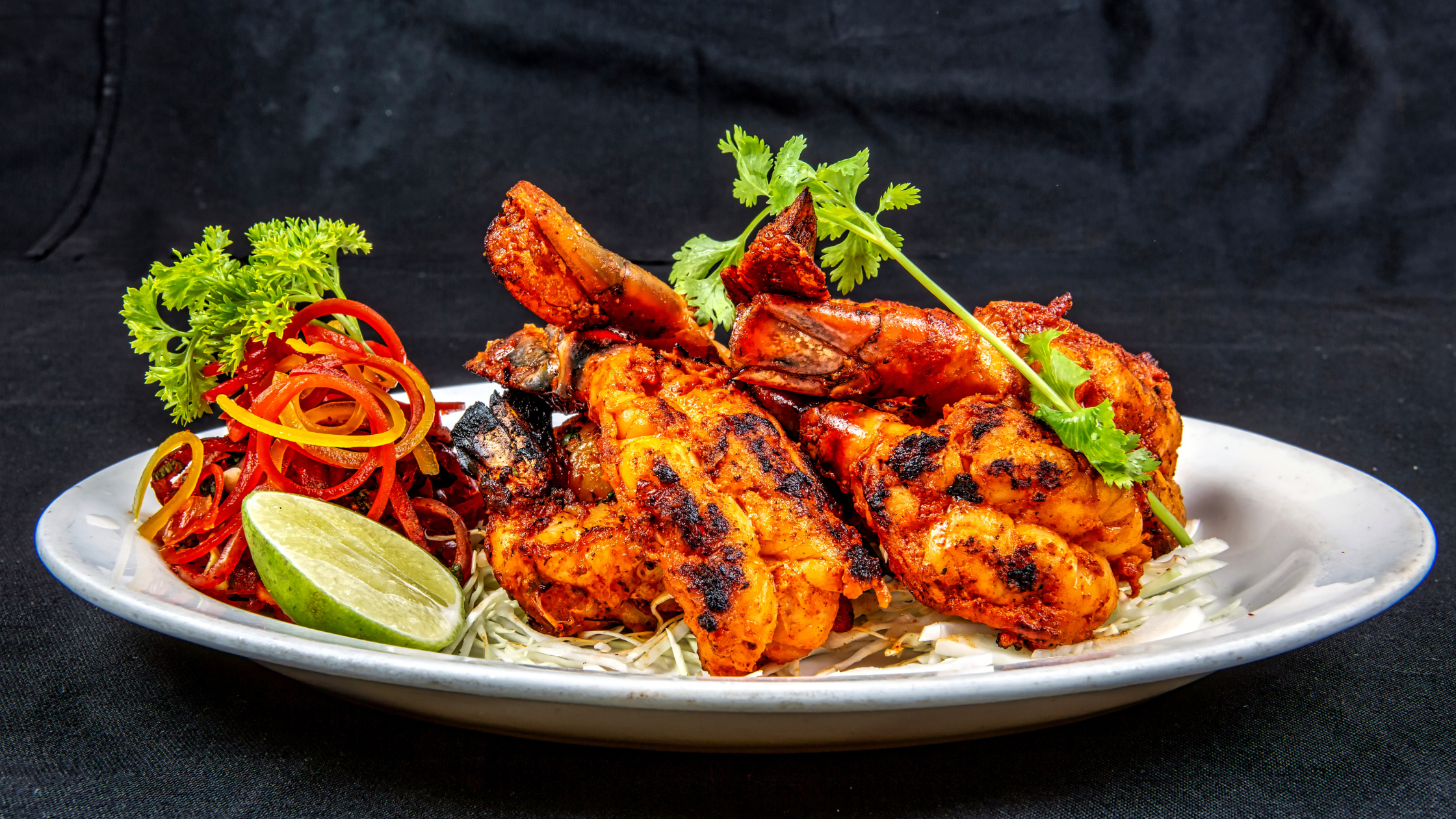 Chicken Tandoori served in a White plate with slices of lemon, corriander leaf and onion