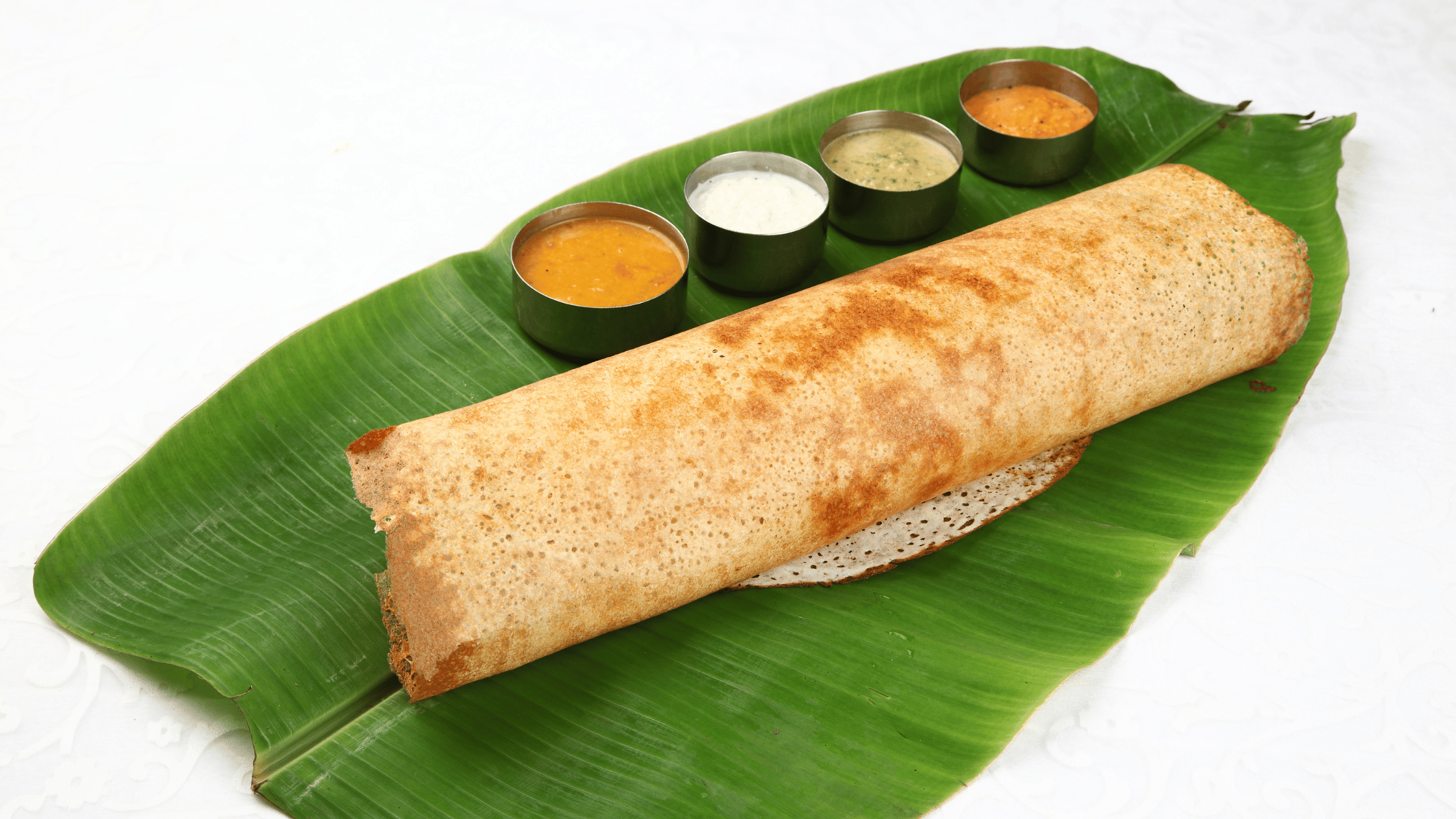 Dosa served in banana leaf with Coconut Chutney, Tomato Chutney. Mint Chutney and Tamarind Chutney