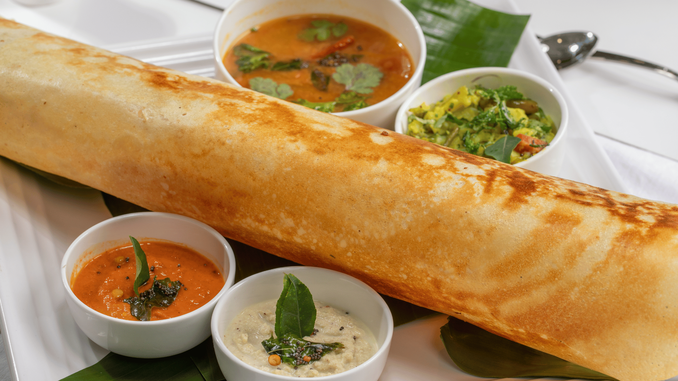 Dosa served in plate with Sambhar, Coconut Chutney, Tomato Chutney and Mint Chutney