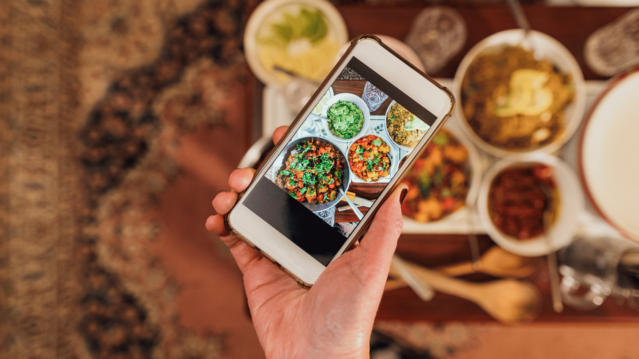 Person holding a smartphone capturing a photo of vibrant South Indian dishes on a table, including curries, rice, and chutneys. Perfect for showcasing the flavors and variety of a local South Indian restaurant.