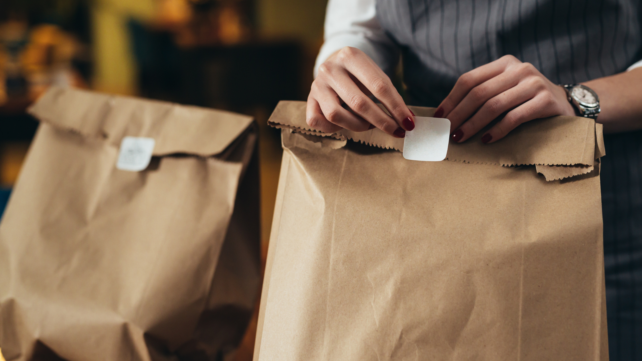 Close-up of a person sealing brown paper bags with stickers, representing takeout packaging. The banner highlights the theme "Best Indian Takeout Food Near Me," symbolizing convenient and secure food delivery.