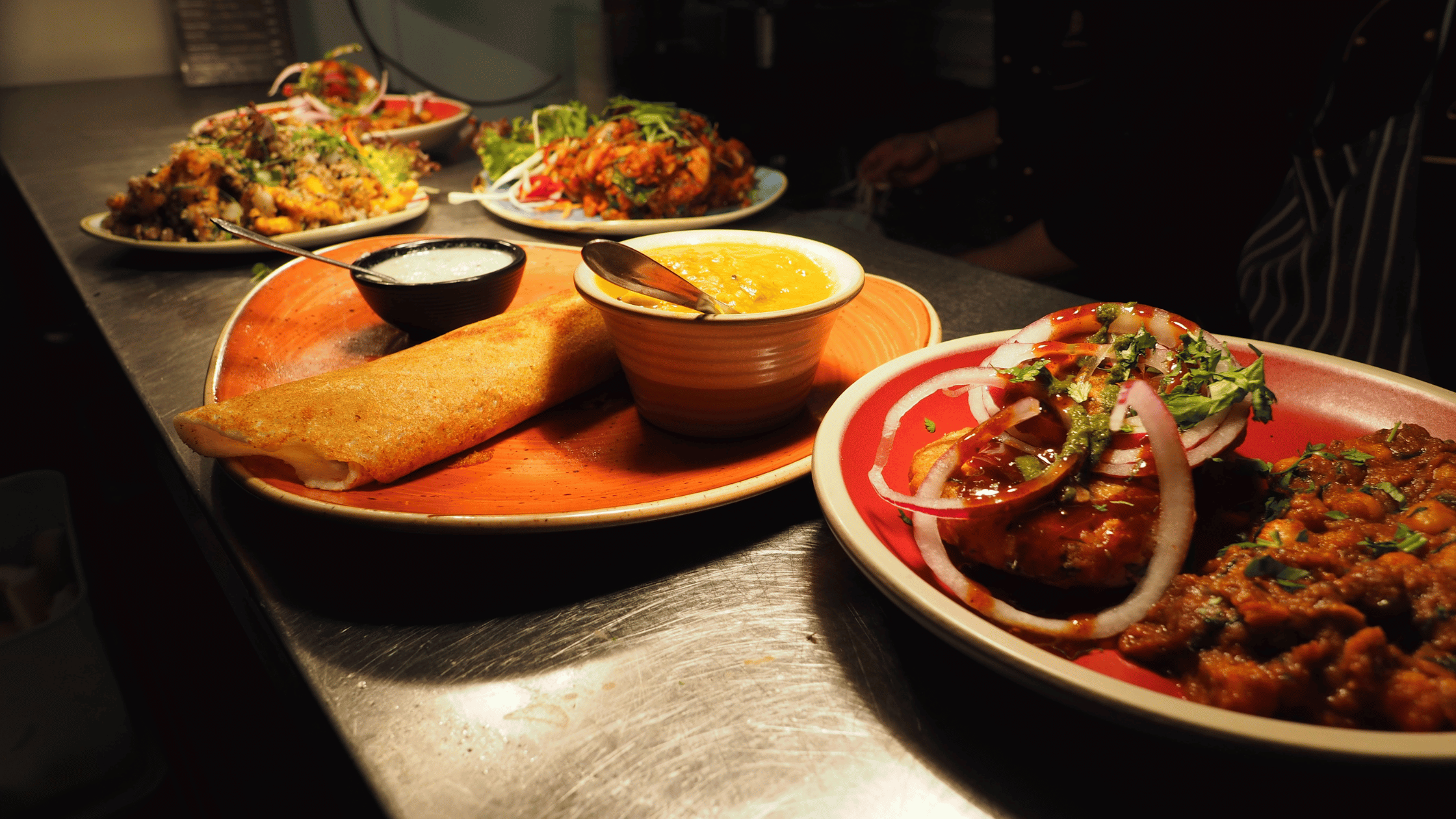 Authentic Indian cuisine served fresh on colorful plates, featuring dosa with chutneys, chole, and tandoori dishes – traditional South Indian and North Indian flavors at their best